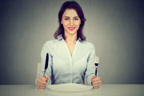 Vrouw met mes en vork aan tafel met leeg bord