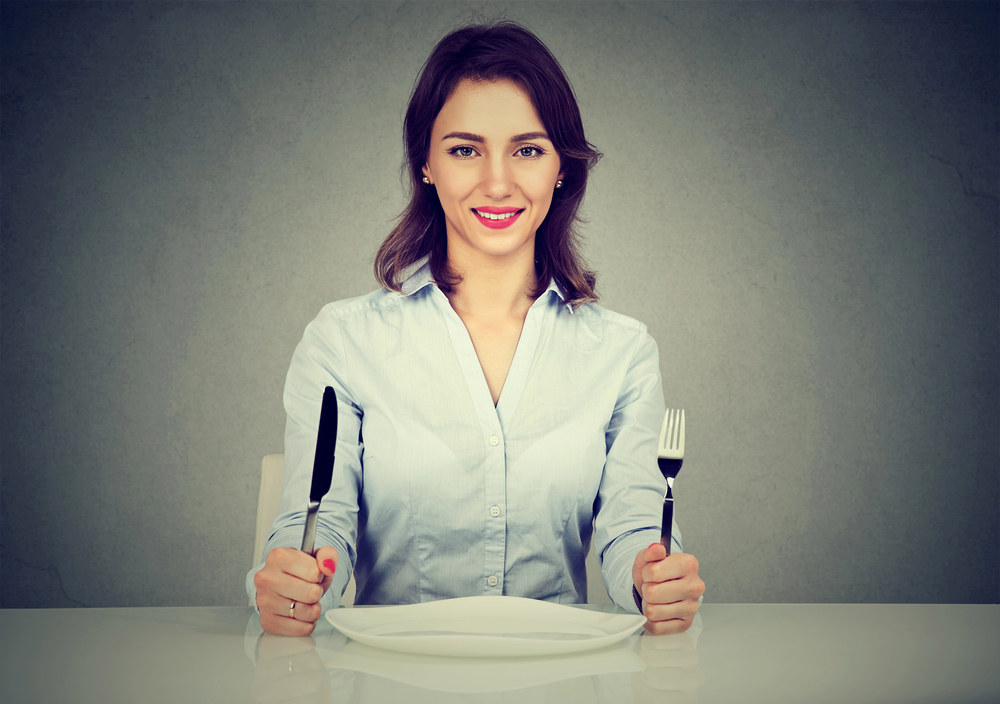 Vrouw met mes en vork aan tafel met leeg bord